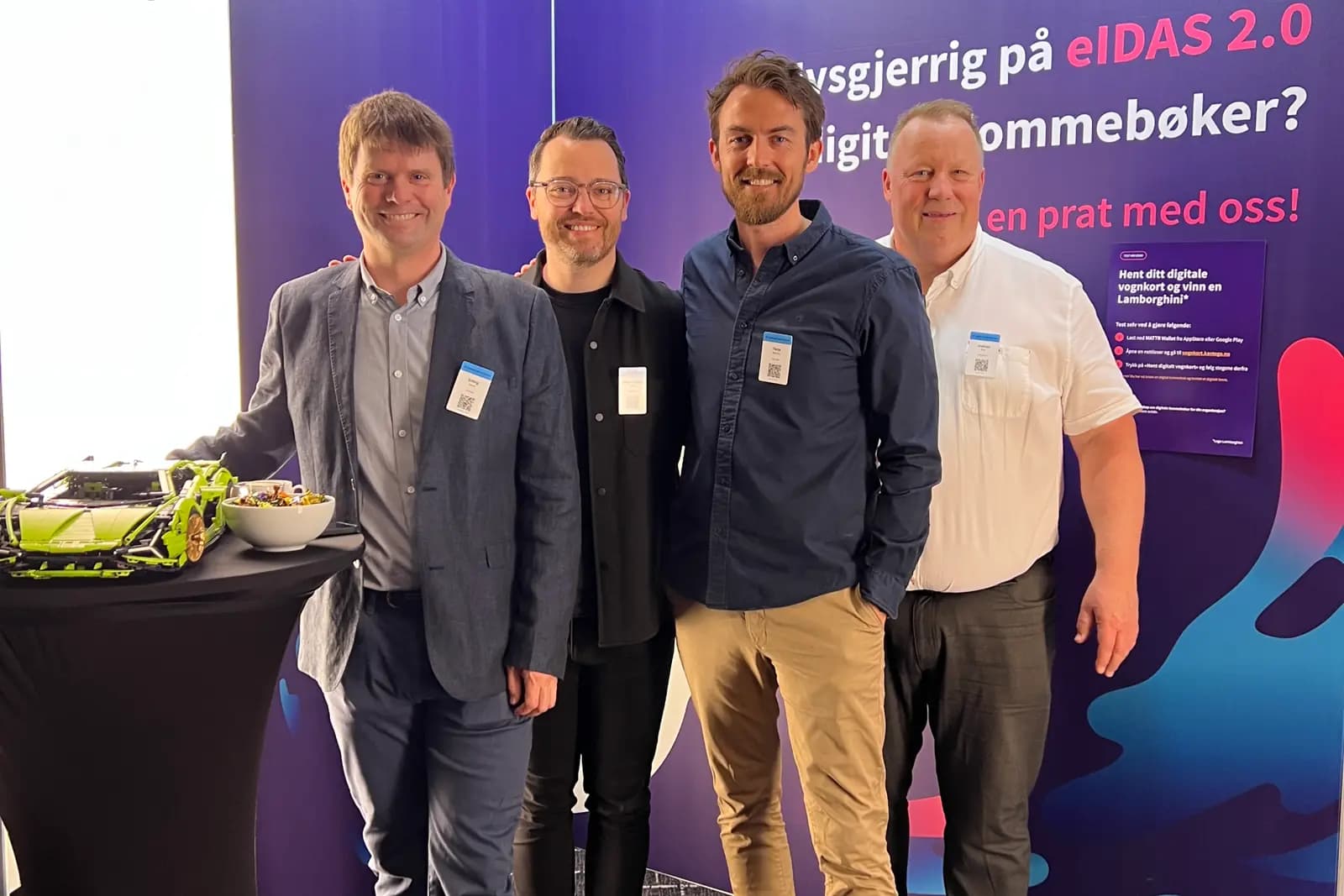Fire menn står foran en stand med teksten «Nysgjerrig på eIDAS 2.0 og digitale lommebøker?»
